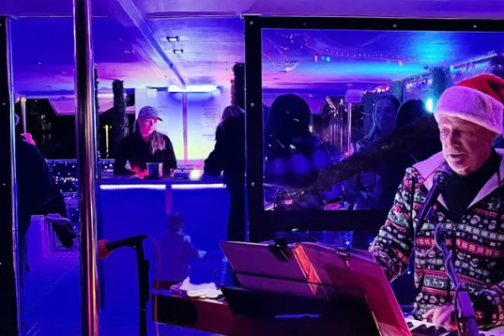 Person in festive attire playing keyboard on a decorated stage with colorful lights.