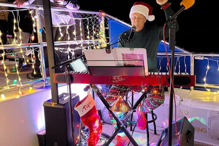 Man in Santa hat playing keyboard on decorated stage with Christmas lights.