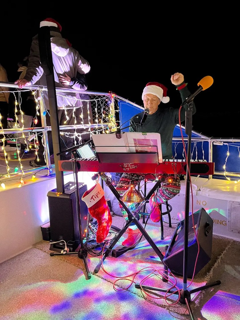 Musician in a Santa hat playing keyboard on a boat decorated with holiday lights