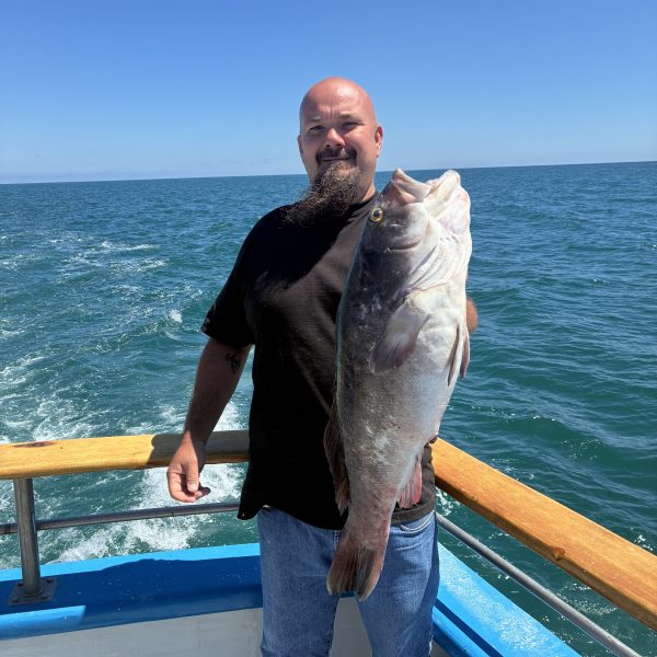 Man holding large fish on a boat, ocean in the background.