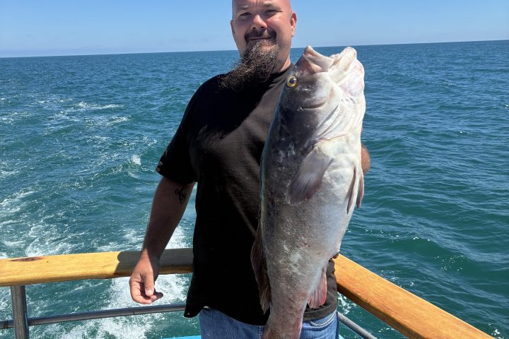 Man holding large fish on a boat, ocean in the background.