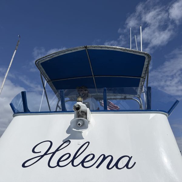 Boat named Helena reflected upside down in calm water.