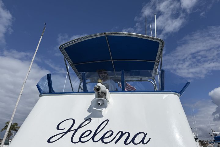 Boat named Helena reflected upside down in calm water.