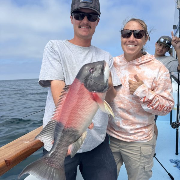 Two people on a boat holding a large fish, smiling.