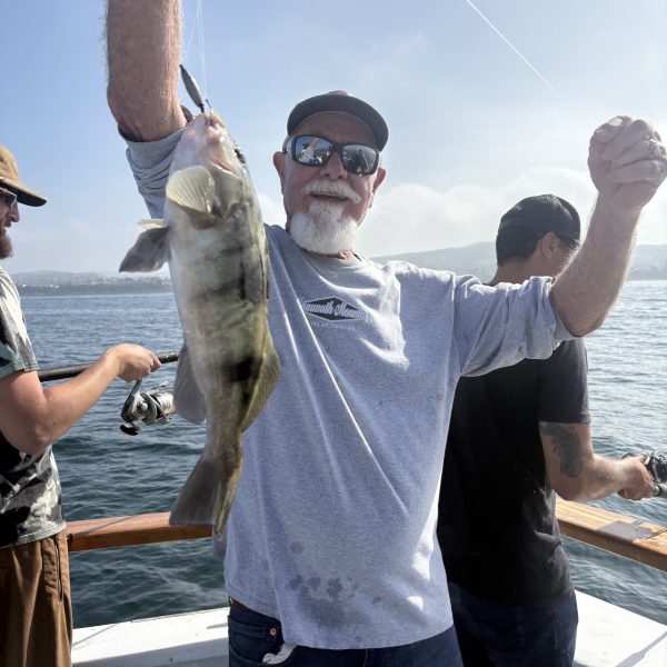 Man on boat holding a fish, smiling, with ocean in background.