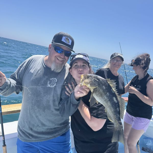 Group of people on a boat, two holding a fish, sunny day.