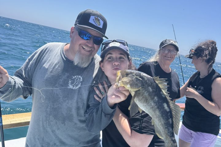 Group of people on a boat, two holding a fish, sunny day.