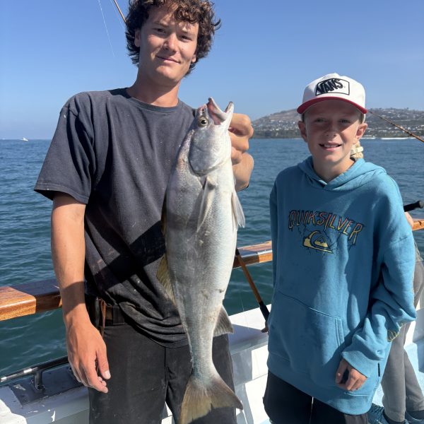 Two people on a boat holding a large fish, with a blue ocean background.