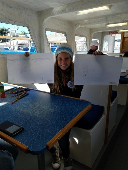 Young artist holding up her whale drawings after the Wyland art lesson on board