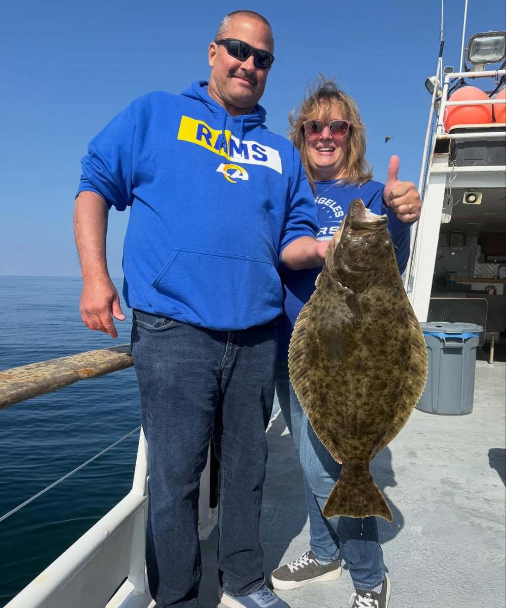 Two people on a boat holding a large fish, with the ocean in the background.