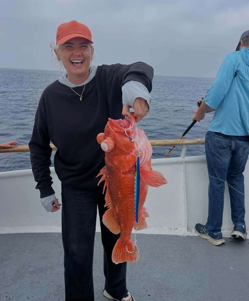Person in cap holding a large orange fish on a boat with ocean in background.