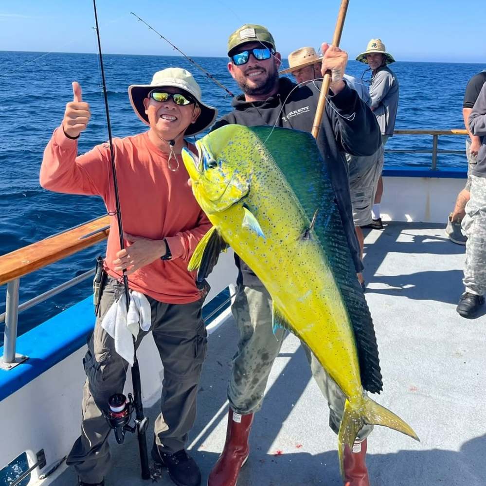 Two people on a boat holding a large mahi-mahi fish, one giving a thumbs up.