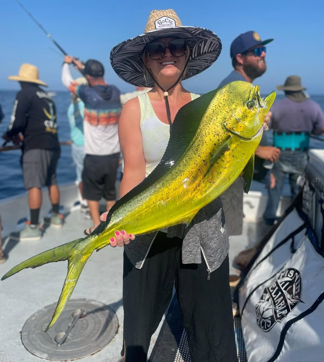Woman holding a large yellow fish on a boat with several other people fishing.