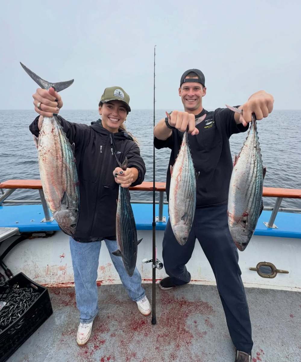 Two people on a boat holding freshly caught fish with smiles.