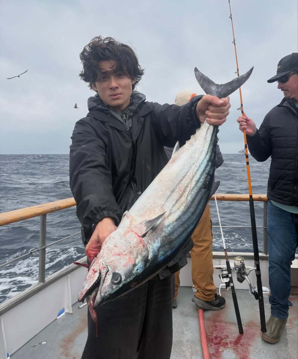 Person holding a large fish on a boat at sea, with fishing rods in the background.