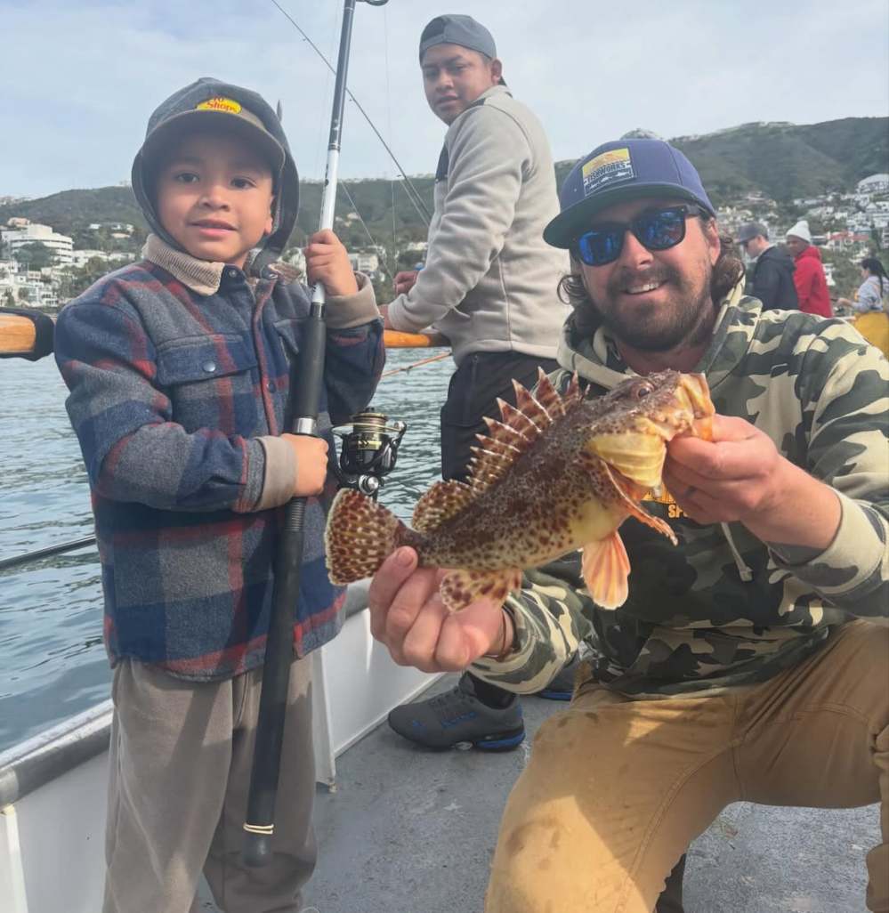 Child holding a fishing rod and man showing a spiky fish on a boat, with another person in the background.