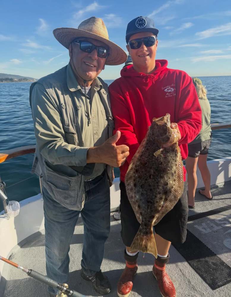 Two people on a boat holding a large fish, one giving a thumbs up.