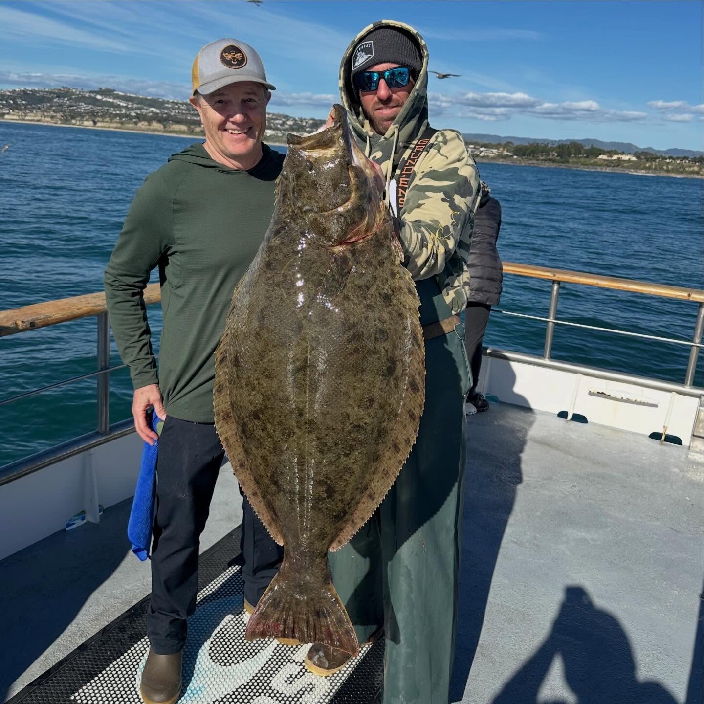 Two people holding a large flat fish on a boat with the ocean in the background.