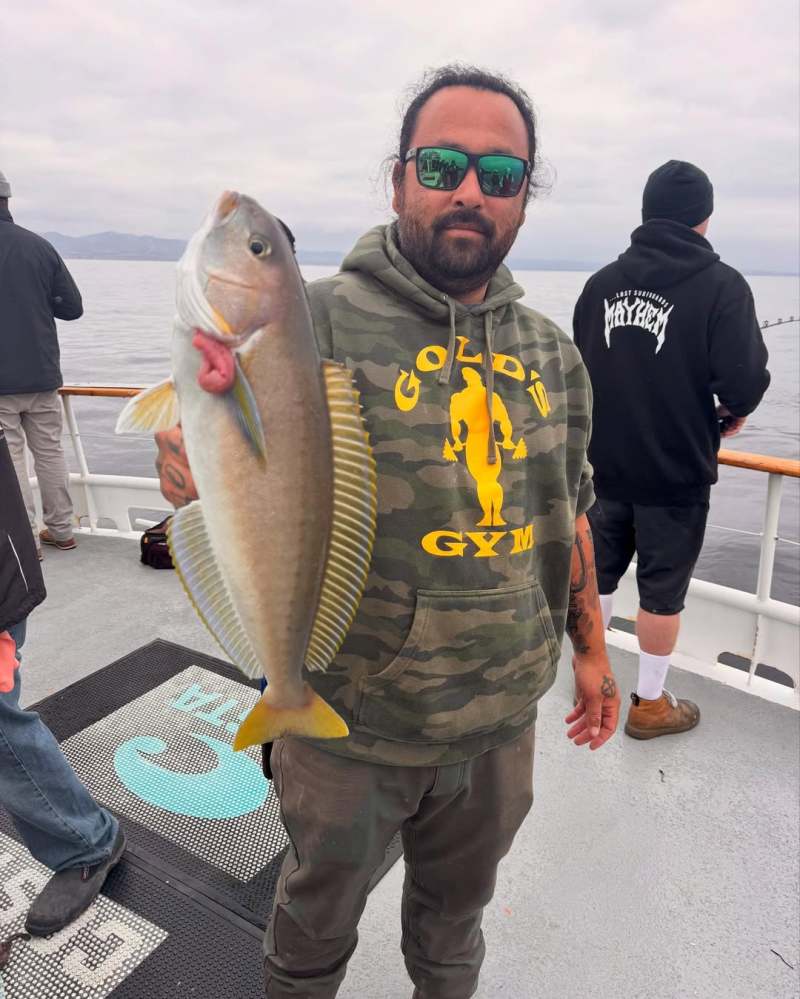 Man holding a fish on a boat deck, wearing sunglasses and a camo hoodie.