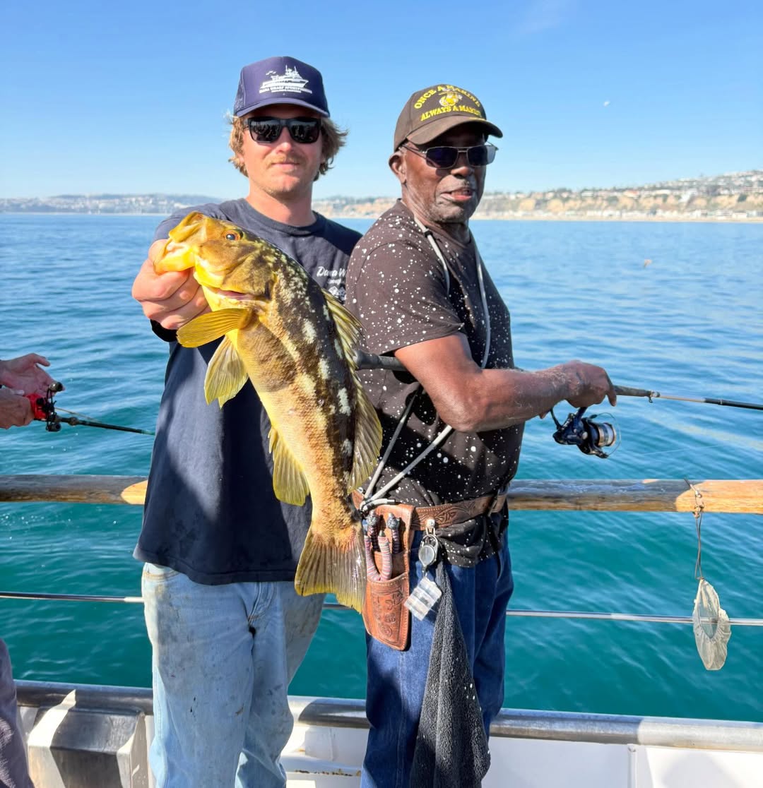 Two men on a boat holding a large fish on a sunny day.