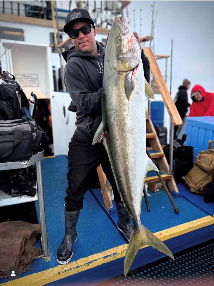 Person on a boat holding a large fish vertically, with fishing gear visible.