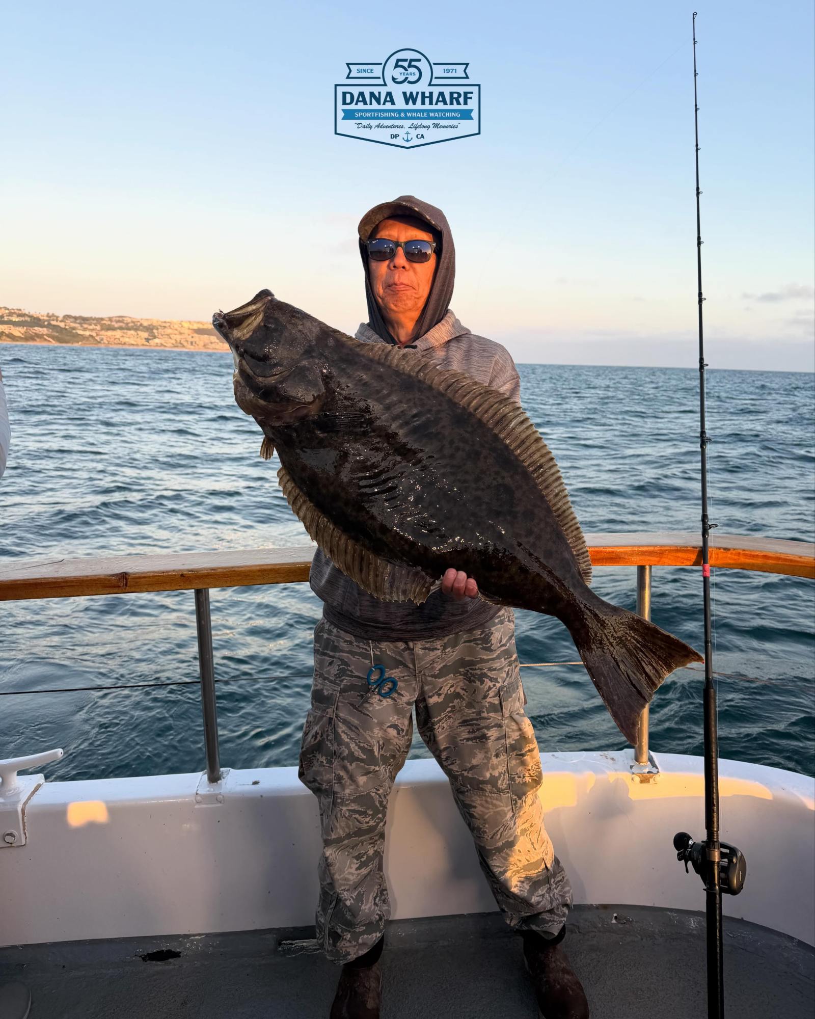 Angler holding a large halibut on a Dana Wharf sportfishing boat at sunset
