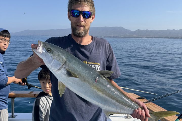 Man on boat holding a large fish, with a calm sea in the background.