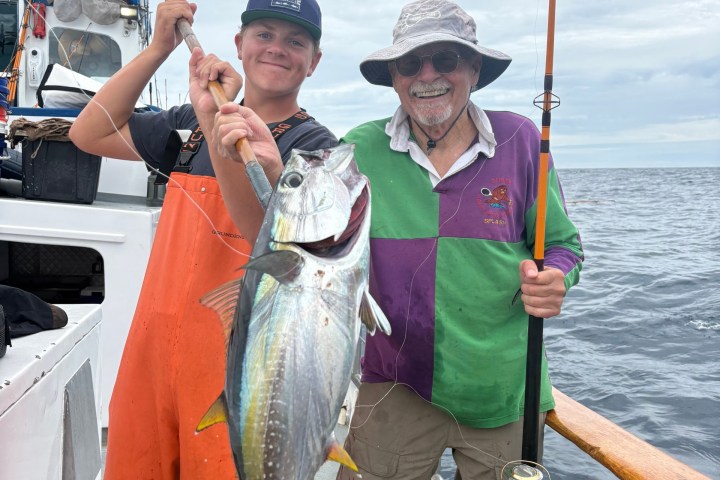 Two people on a boat holding fishing rods and a large fish.