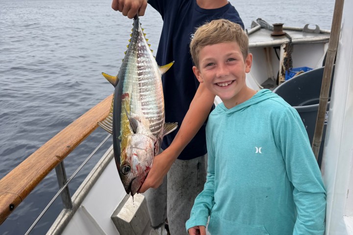 Two smiling boys on a boat holding a large fish.