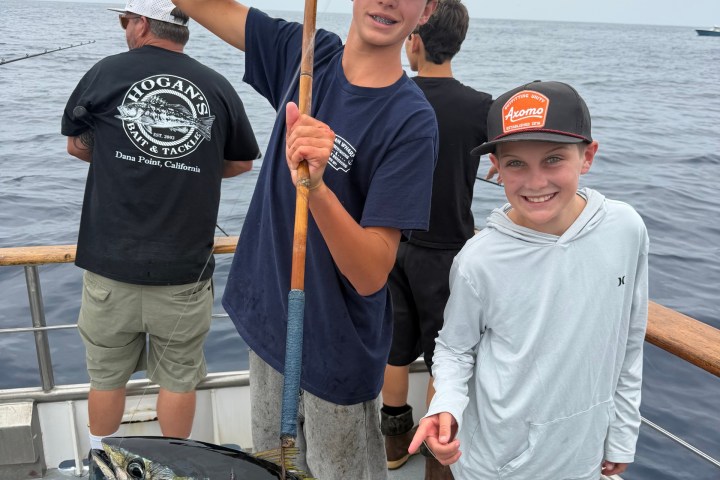 Two boys on a boat holding a large fish, with ocean in background.