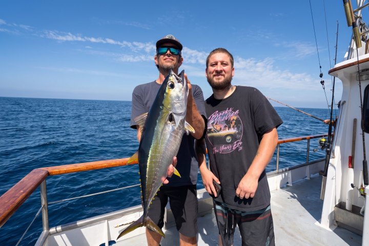 Angler holding a tuna beside a friend on a Dana Wharf 10-hour offshore fishing trip