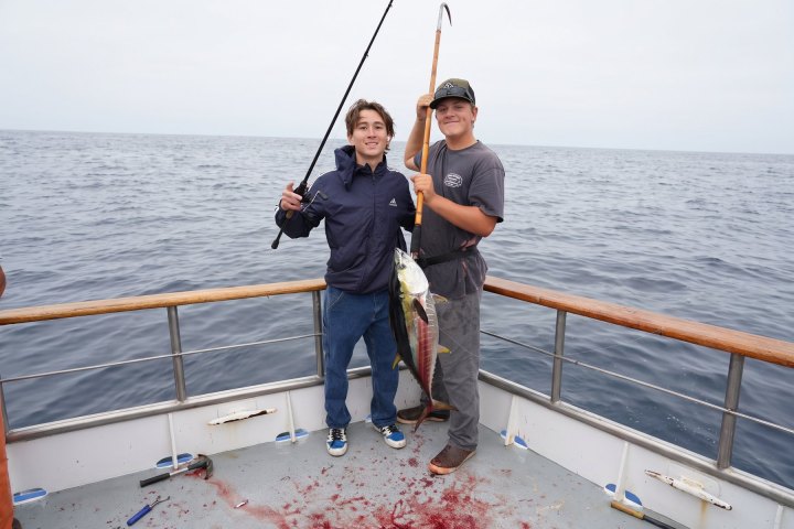 Two people holding fishing rods and a caught fish on a boat.
