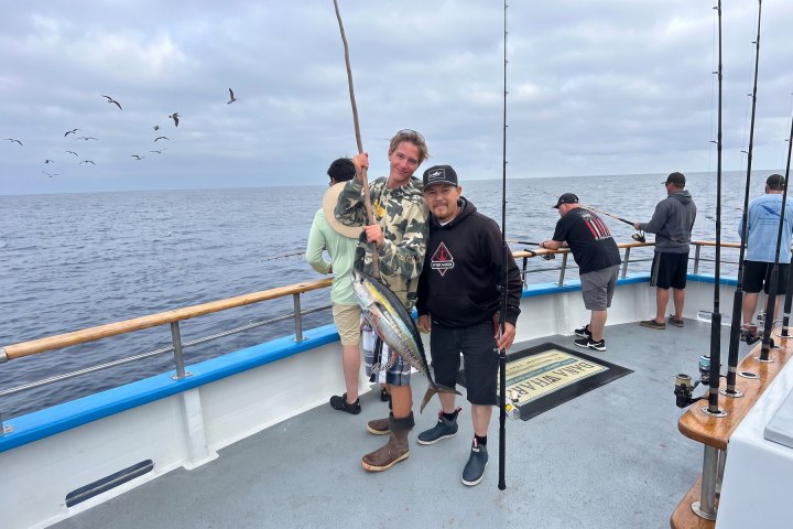 Two people on a boat holding a freshly caught fish.
