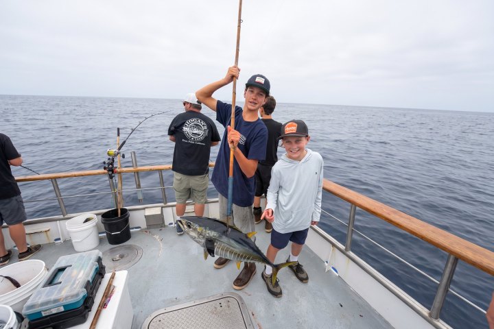 Two boys on a boat holding a large fish, with ocean in background.