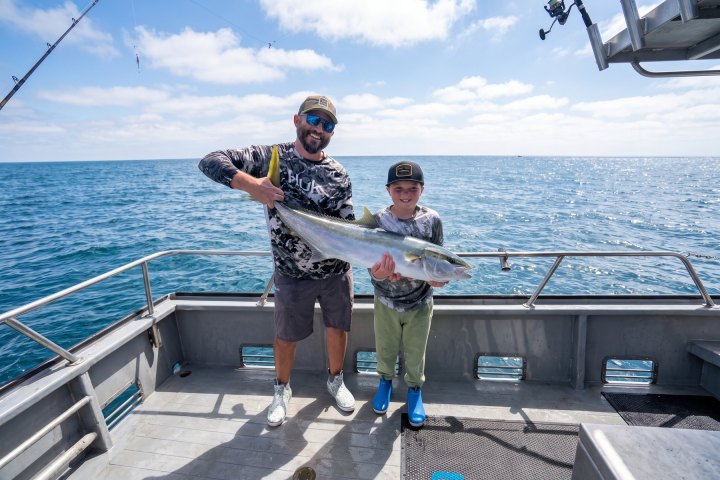 Two anglers, one adult and one young, with a yellowtail on a Dana Wharf all-day fishing trip