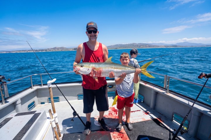 Two anglers, one adult and one young, with a yellowtail on a Dana Wharf all-day fishing trip